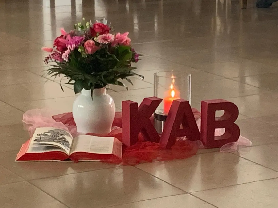 Blumenvase mit rosa Gerbera und Rosen, eine Bibel und KAB Buchstaben auf einem Tuch