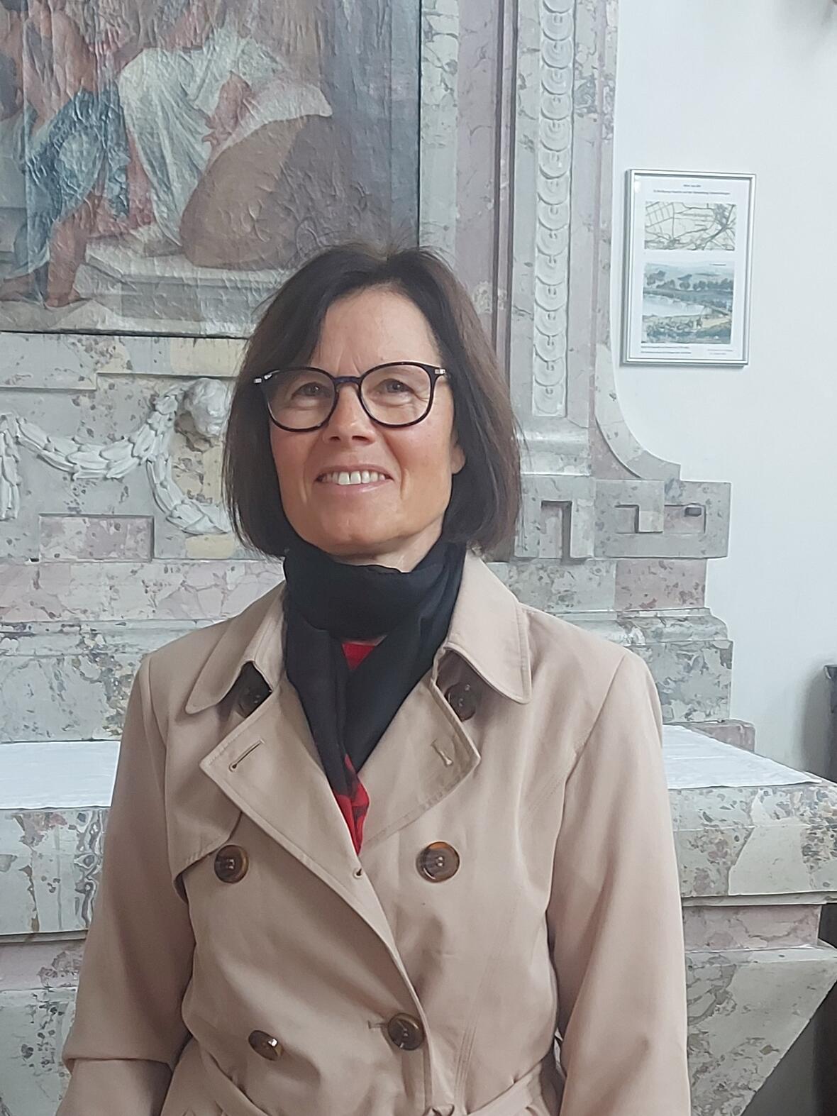 Sandra Lötterle Frau lächelnd, lange dunkle Haare und Brille steht in der Kirche vor einem Seitenaltar