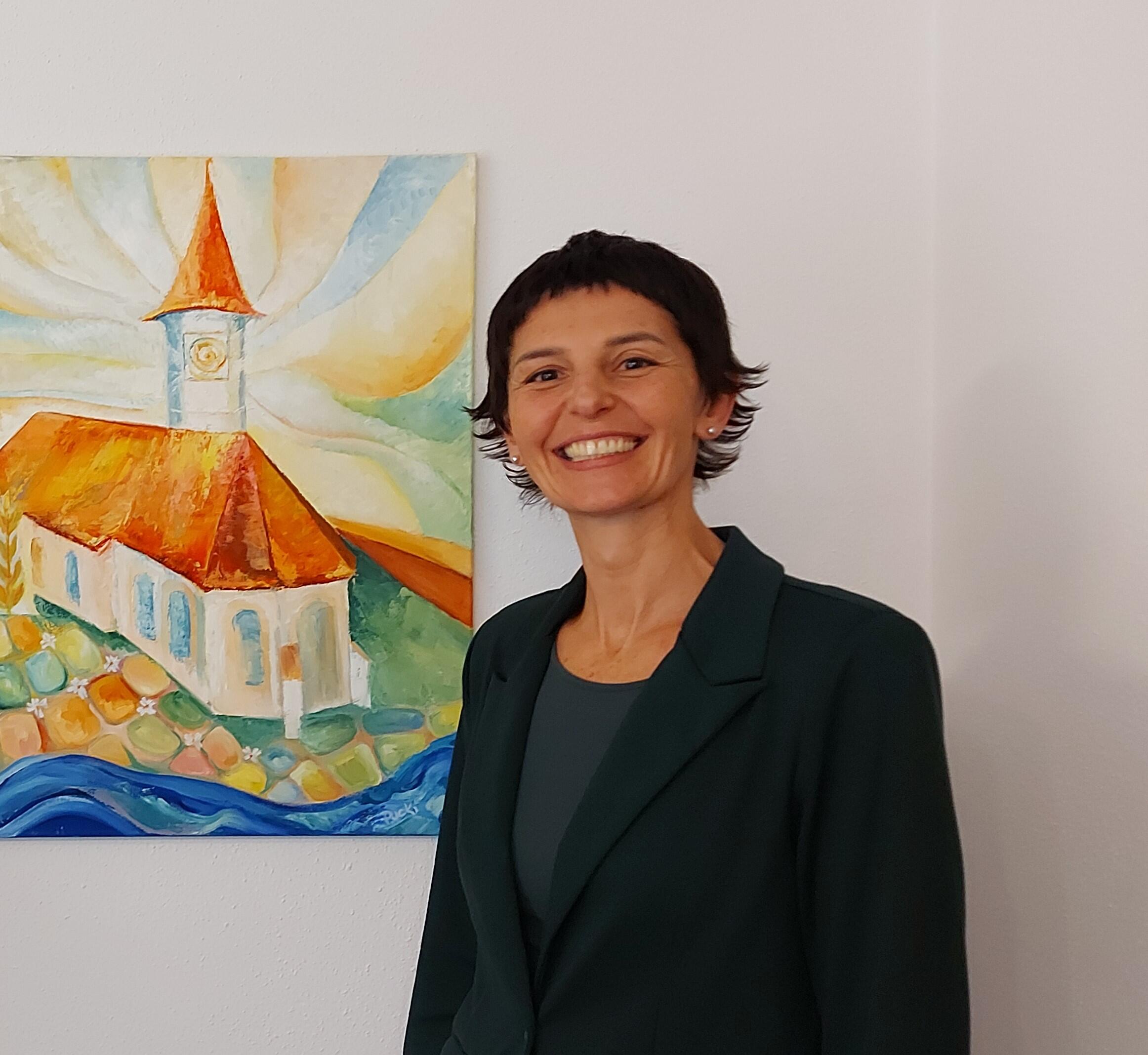 Frau steht lächelnd vor einem Bild von der Kirche St. Laurentius. Sie hat kurze schwarze Haare