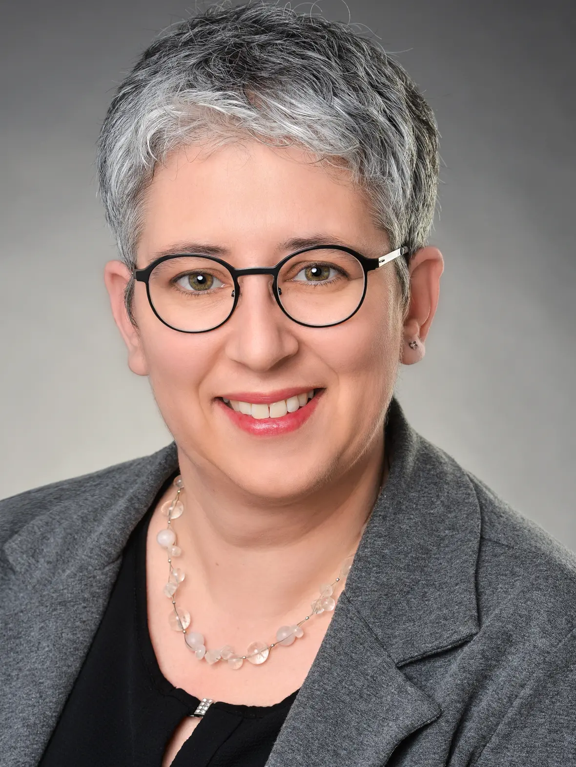 Sandra Schweizer, Verwaltungsleitung, lächelt freundlich in einem grauen Blazer mit Ohrsteckern.