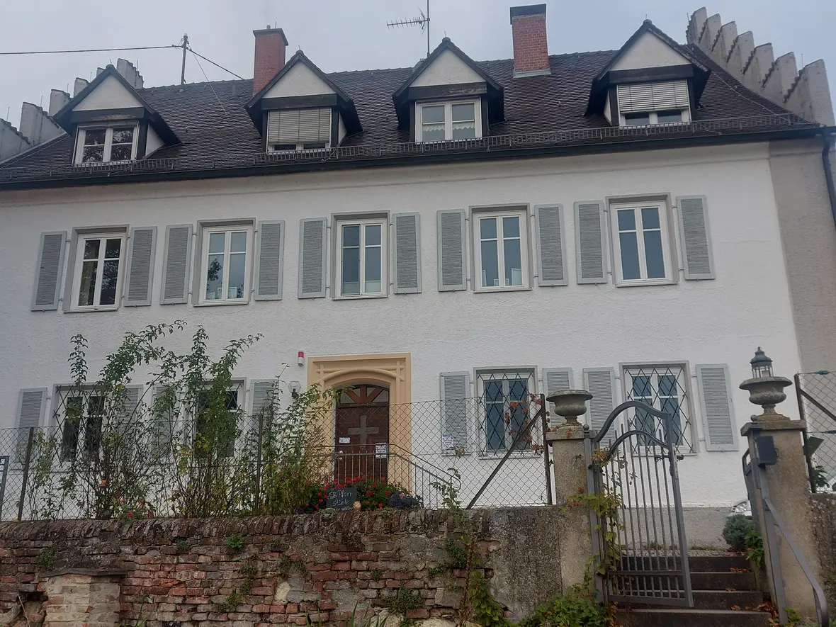 Pfarrhaus Oberelchingen mit hellem Fassadenanstrich und grünen Fensterläden. Garten mit Bepflanzung.
