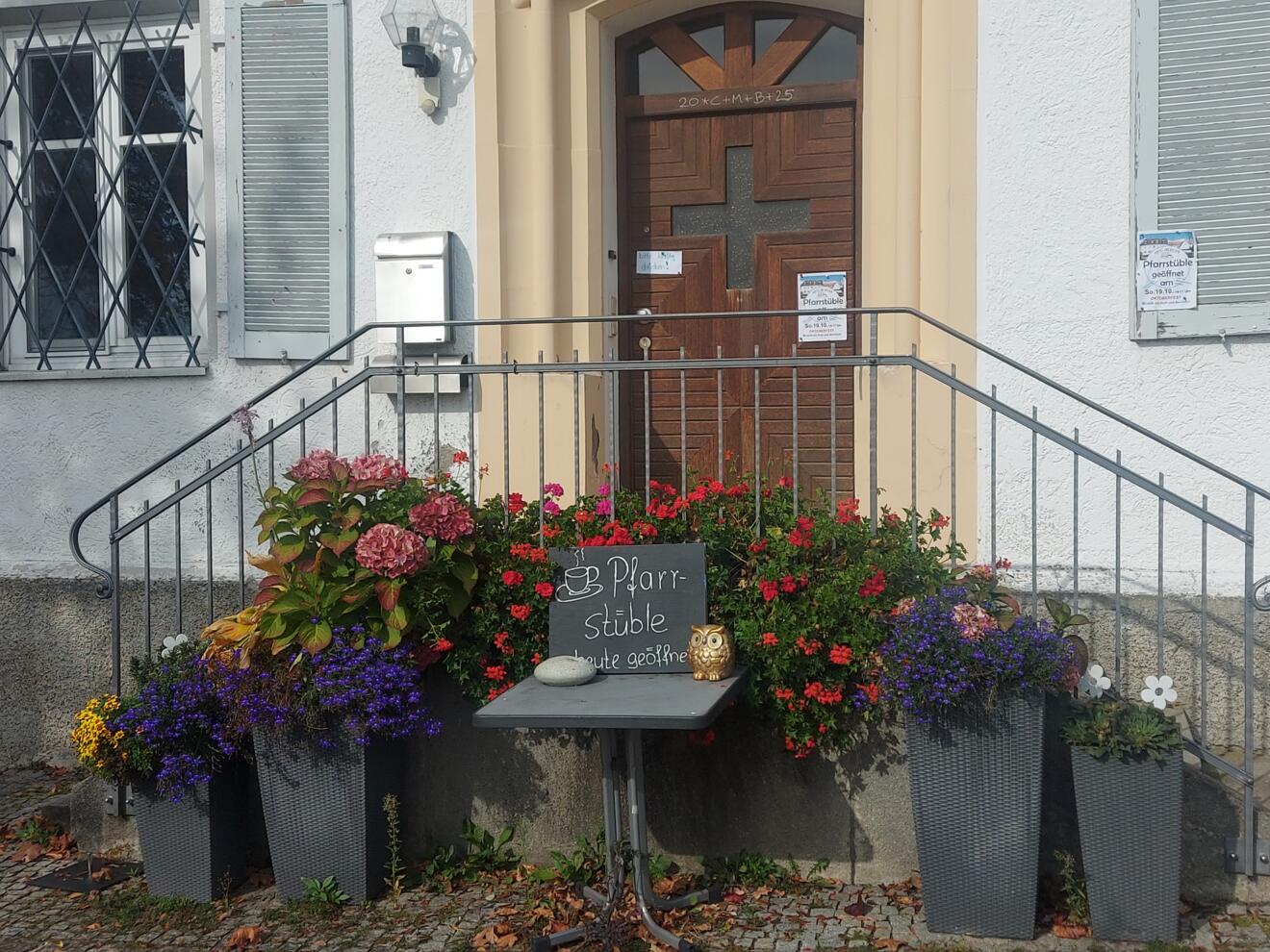 Pfarrhaus Oberelchingen mit blühenden Pflanzen vor der Haustür und einem Schild zur Pfarrstube.