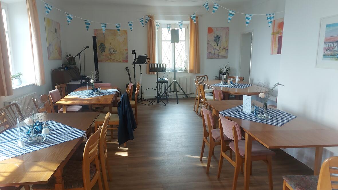 Gemütlicher Raum im Pfarrhaus Oberelchingen mit Tischen, Dekoration und Bühne für Veranstaltungen.