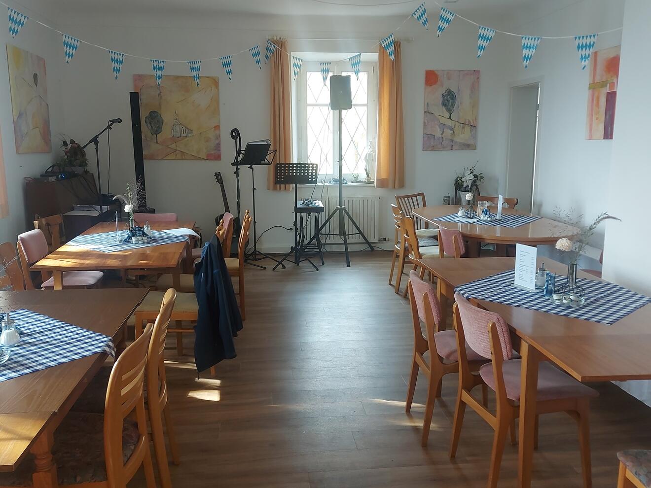 Gemütlicher Raum im Pfarrhaus Oberelchingen mit Tischen, Dekoration und Bühne für Veranstaltungen.