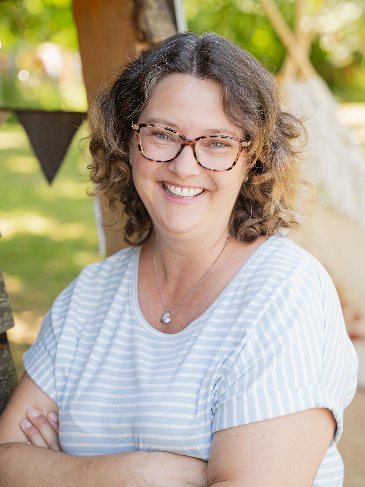 Jenny Beck-Balkheimer Jenny Beck-Balkheimer lächelt in einem Garten, umgeben von Natur und Dekorationen.