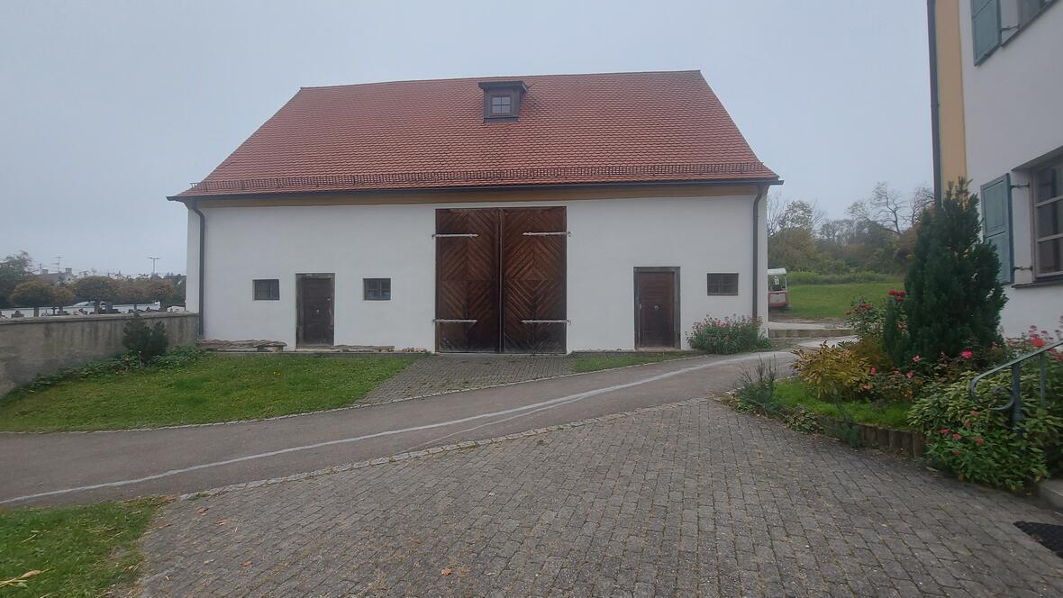 Streifenförmige Holztore an einem weißen Gebäude mit roten Dach, umgeben von Grünflächen.