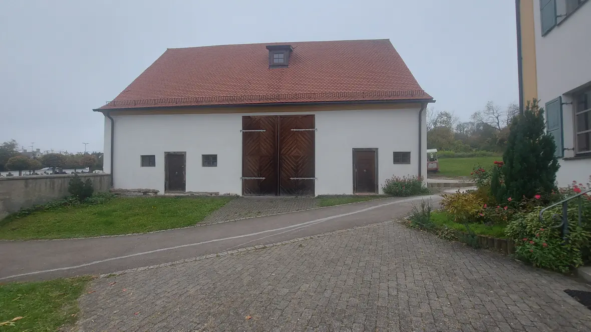 Streifenförmige Holztore an einem weißen Gebäude mit roten Dach, umgeben von Grünflächen.