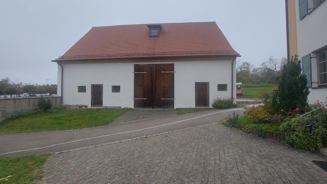 Streifenförmige Holztore an einem weißen Gebäude mit roten Dach, umgeben von Grünflächen.