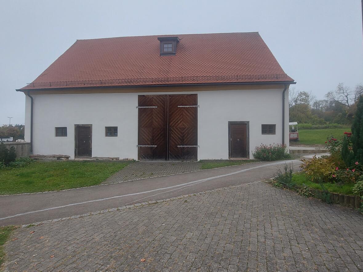 Streifenförmige Holztore an einem weißen Gebäude mit roten Dach, umgeben von Grünflächen.