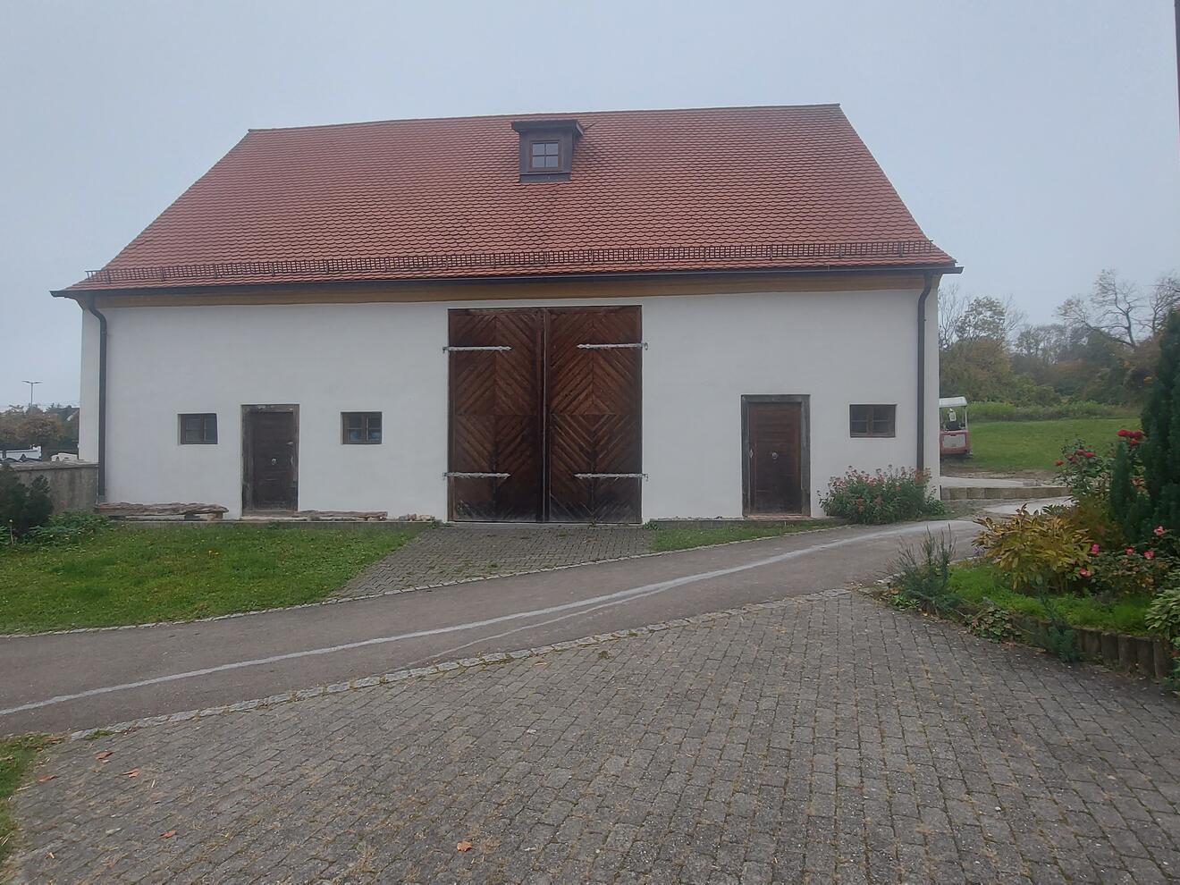 Streifenförmige Holztore an einem weißen Gebäude mit roten Dach, umgeben von Grünflächen.