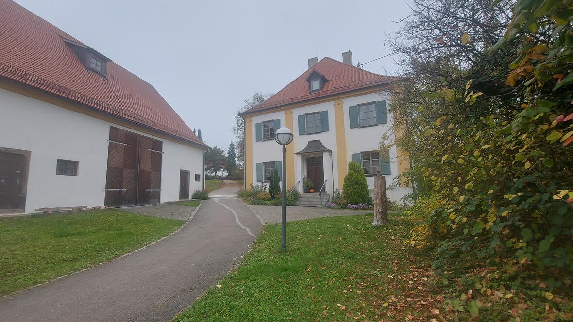 Stadel und Michaelshaus mit grünem Rasen und einem Weg, umgeben von Bäumen und Gebäuden.