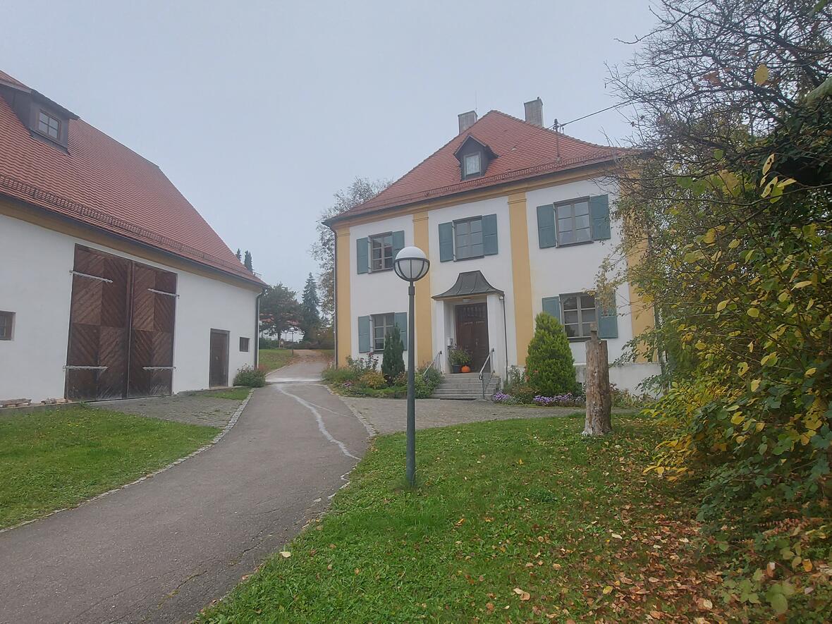 Stadel und Michaelshaus mit grünem Rasen und einem Weg, umgeben von Bäumen und Gebäuden.