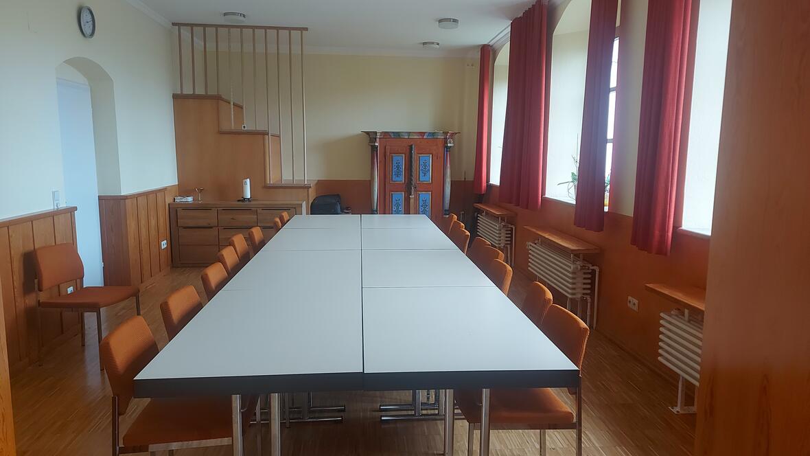 Besprechungsraum mit großem Tisch, orangefarbenen Stühlen und Holzverkleidung.