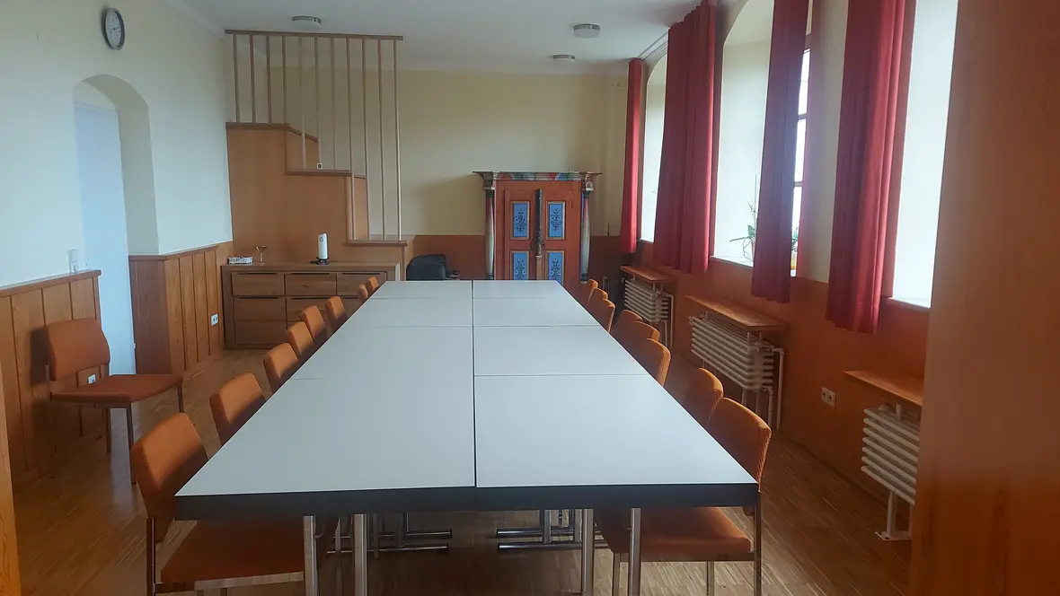 Besprechungsraum mit großem Tisch, orangefarbenen Stühlen und Holzverkleidung.