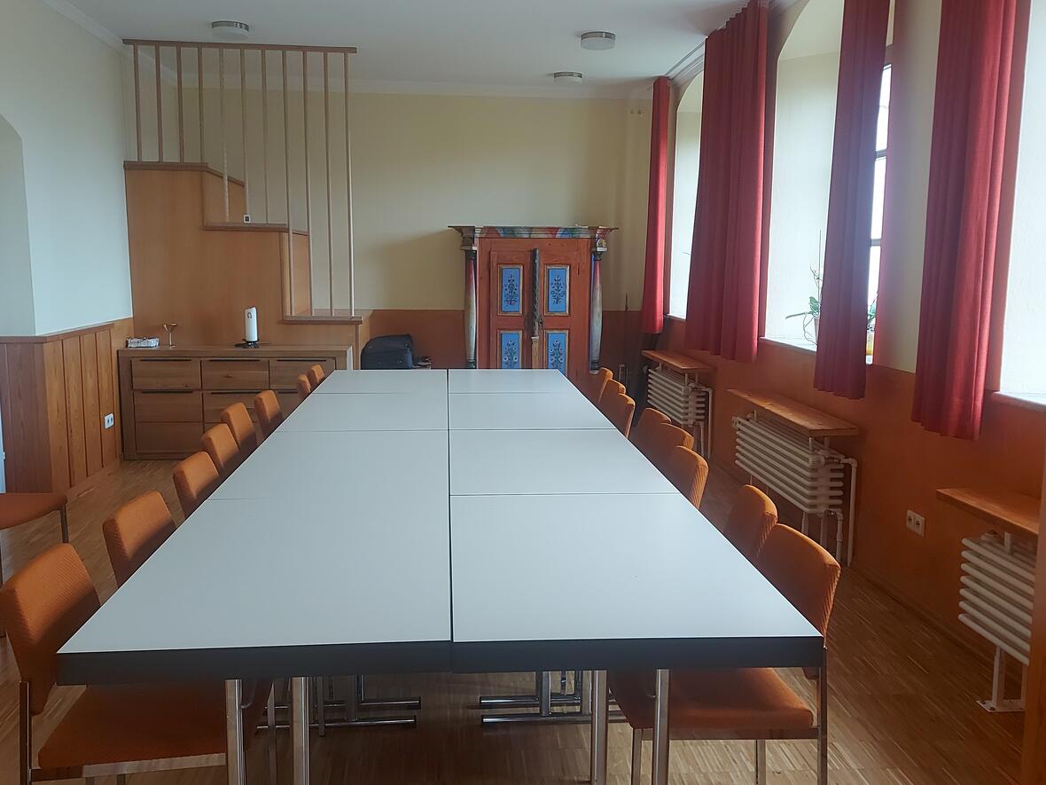 Besprechungsraum mit großem Tisch, orangefarbenen Stühlen und Holzverkleidung.