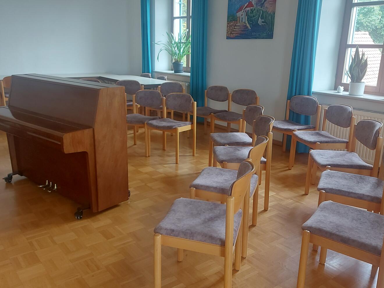 Ein Raum mit einem Klavier und mehreren Stühlen, umgeben von Pflanzen und Fenstern.